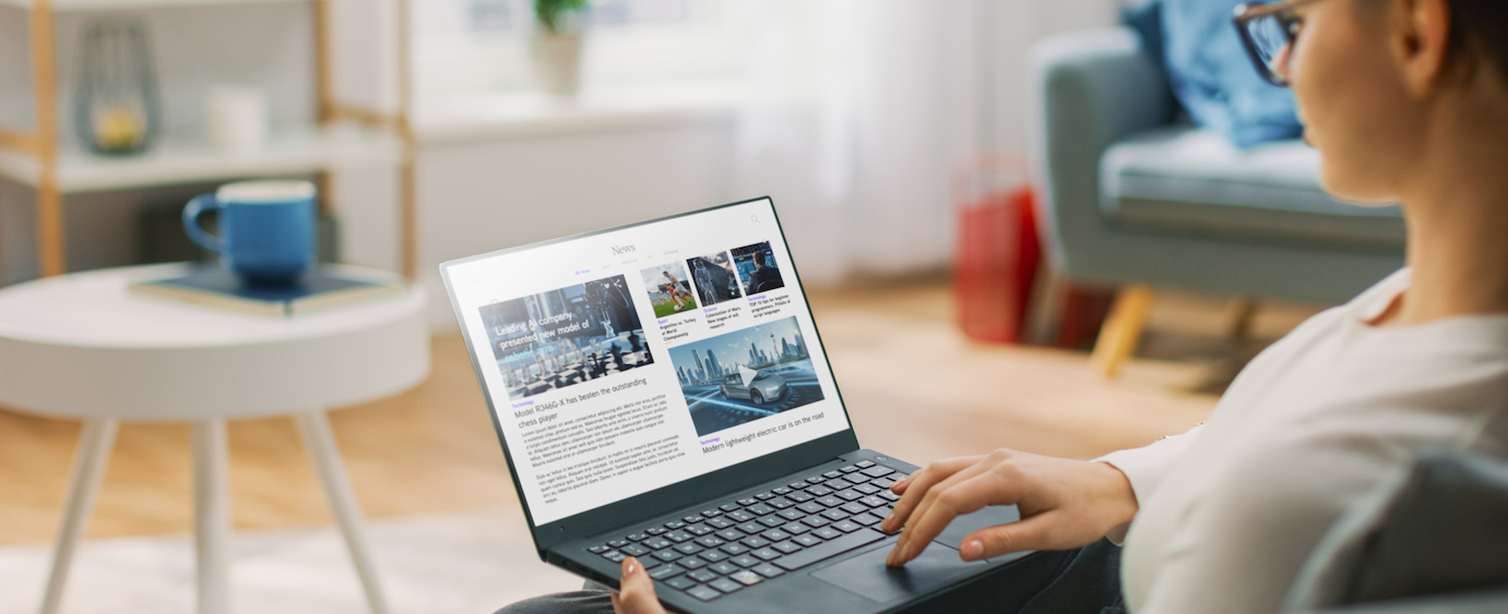 Young Woman at Home Is Using Laptop Computer for Scrolling and Reading News about Technological Breakthroughs. She's Sitting On a Couch in His Cozy Living Room. Over the Shoulder Shot