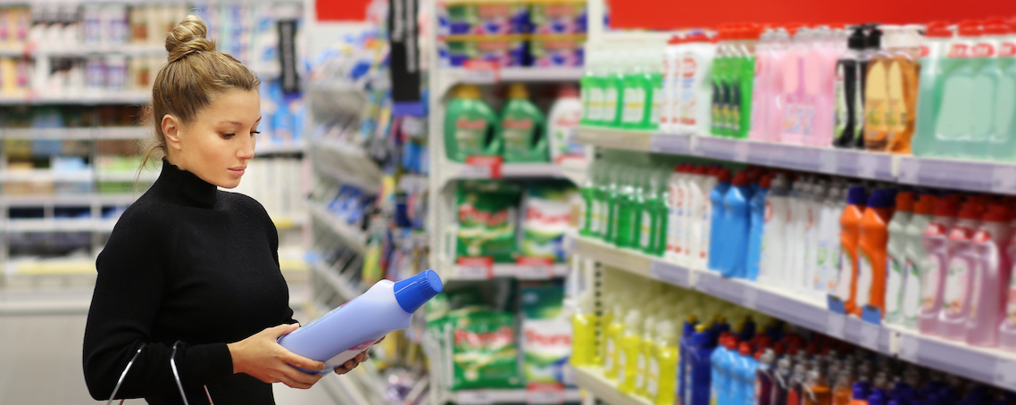 Woman shopping in supermarket reading product information.(shampoo, soap, shower gel,)