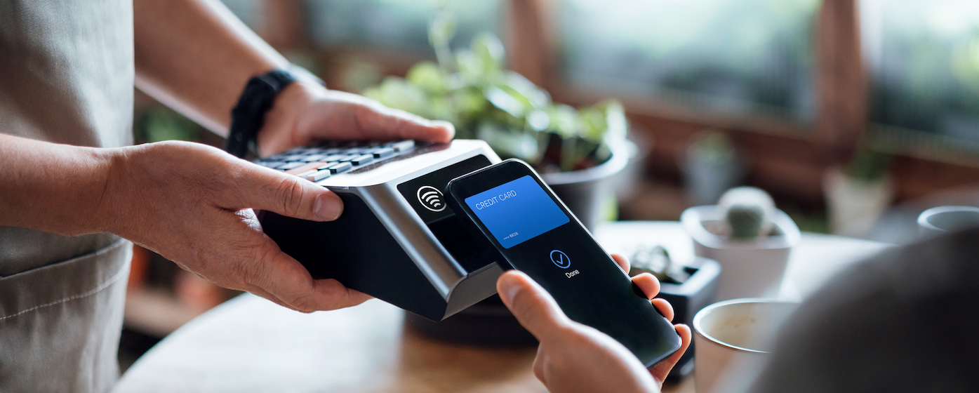 Close up of a male's hand paying bill with credit card contactless payment on smartphone in a cafe, scanning on a card machine. Electronic payment. Banking and technology