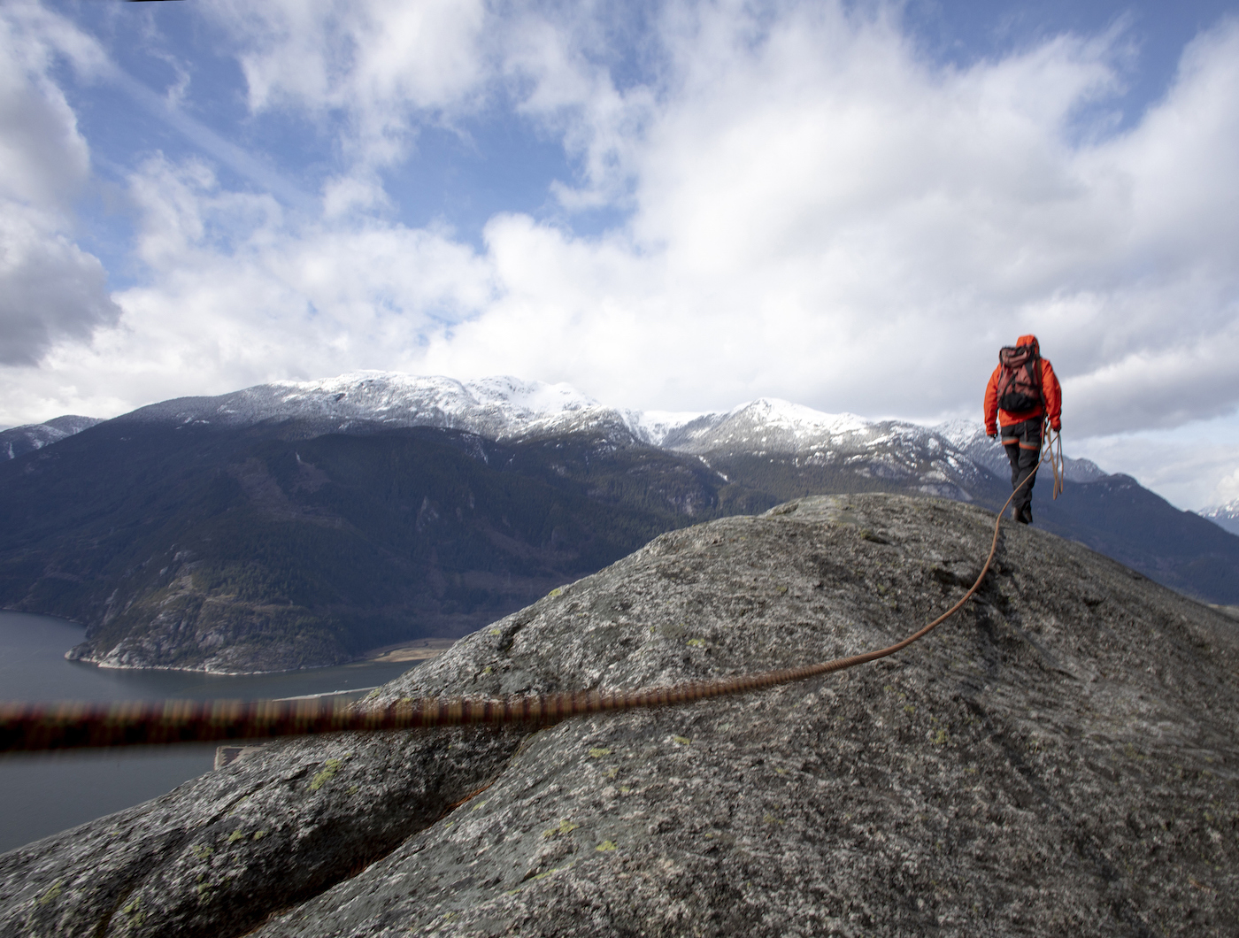 Mountaineer walks along mountain ridge with climbing rope